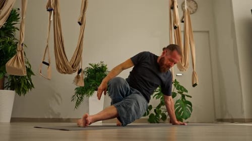 focused adult male yogi with a beard does stretching on the floor meditates and keeps balance