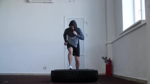 Full Length of Athlete Jumping on Heavy Tire While Exercising in Gym