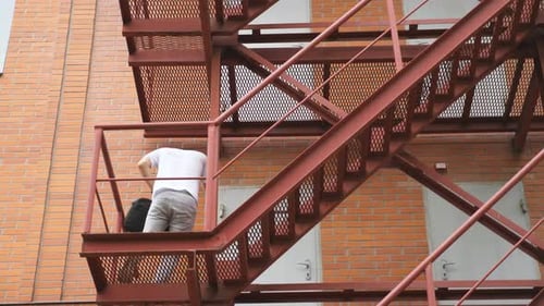 Man Walking Down Fire Escape Talking on Phone