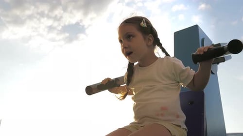 Little Adorable 5Yearold Girl is Engaged on Sport Simulator on the Street Playground in the Sunset