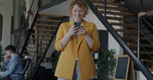Portrait of Happy Businesswoman Using Smartphone Texting Standing in Busy Office
