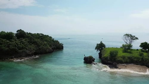 A young man is standing on the edge of a small cliff, looking down in the crystal clear water on a t