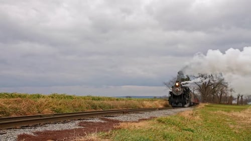 A Low Angle of a Steam Train Puffing Along A Rail Road Track on a Windy Day