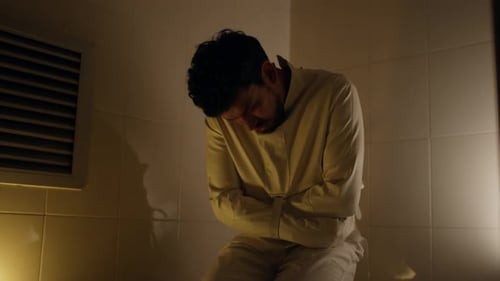 Man in Straitjacket Kneels in Hospital Room at Night