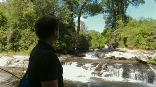 Person steht am ruhigen Fluss im üppigen Wald und blickt auf den Wasserfall