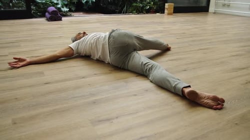 Man Lying on Back Stretching on Wooden Floor