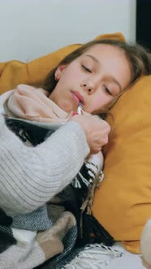 Loving Caring Serious Adult Mom Sitting Near Her Sick Upset Teen Daughter on Sofa and Measuring
