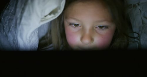 Gros plan d'une petite fille utilisant une tablette ou un smartphone dans le noir sous la couverture. Contre