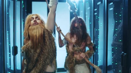 Two Cavemen Stand Closely Together in a Techfilled Server Room