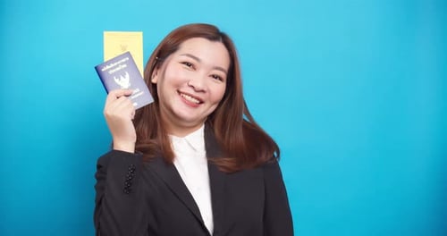 Smiling Woman Holding Two Passports, Standing by Blue Wall