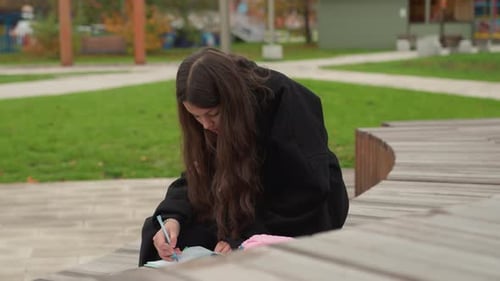 Teen Girl Writing in Notebook Outdoors in Park
