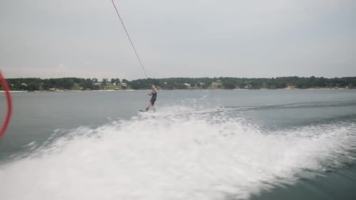 Active Young Wakeboarder Firmly Holding The Rope And Quickly Flipping Into The Air As The Motorboat