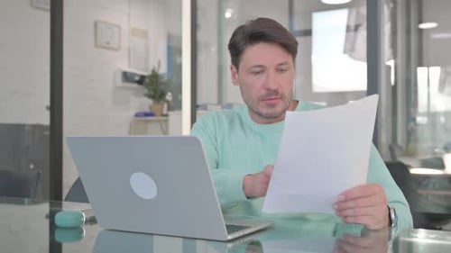 Man Excited About Reading Documents While Using Laptop