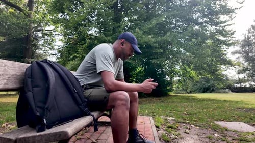 South asian man browsing phone on park bench