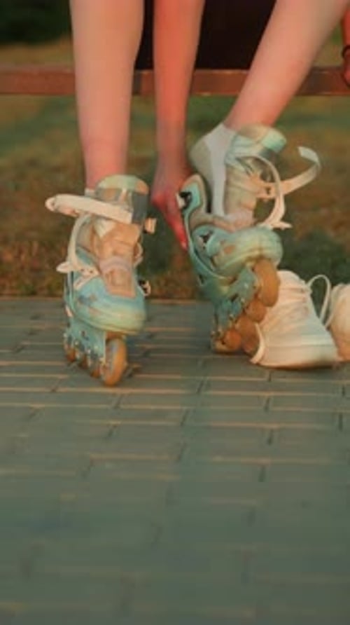 Lady Removing Right Leg Roller Skate During Sunset in Park with Sneakers Beside Her
