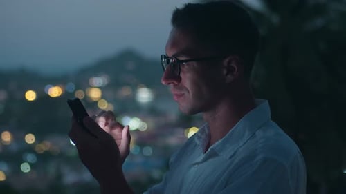 Man Using Phone at Night Overlooking City Lights