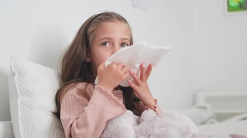 Child with Cold Rests in Bed Blowing Nose