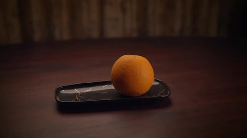 A Hand Placing an Orange on an Elegant Black Tray Creating a Stunning Visual Presentation