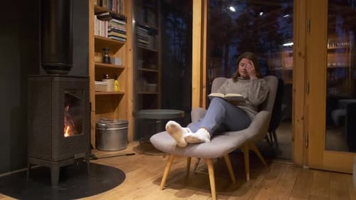 Woman Reading by Fireplace in Cozy Cabin