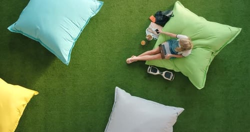 A female student using a laptop and sitting on a bean bag in a library from above