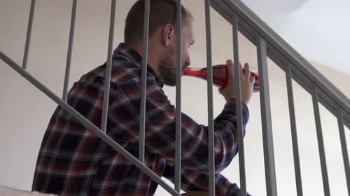 Man Sits on Stairs Drinking From Bottle
