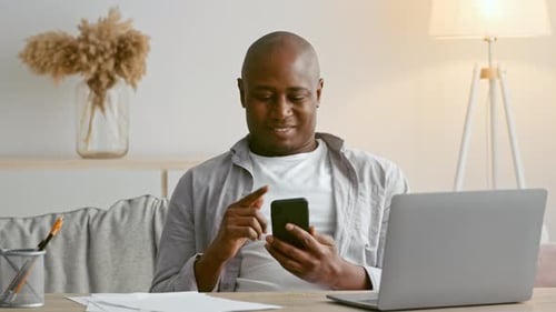 Man Uses Phone and Laptop Indoors