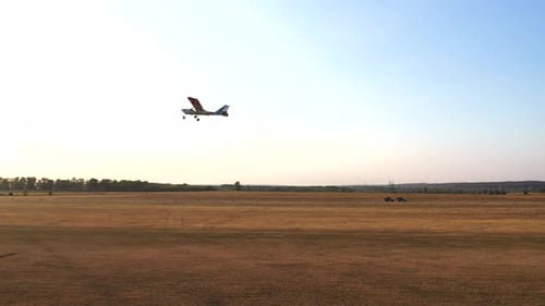 Small Private Airplane Flying Over Airfield with Sun Flares at Background