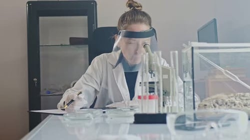 Scientist at Microscope Recording Data in Laboratory