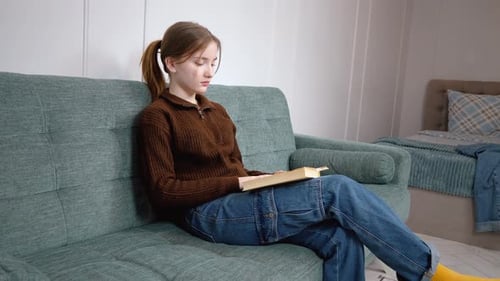Young Woman Reads Book on Couch Indoors