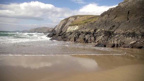 Left pan of Coumeenoole beach in Dingle peninsula, Ireland. Slow motion shot, waves hit rocks, sandy