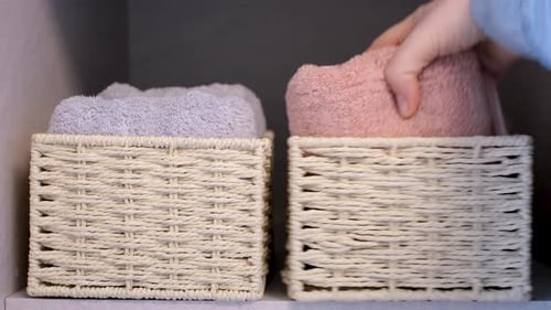 Female hand fold rolled towel into wicker basket standing in the closet close-up.