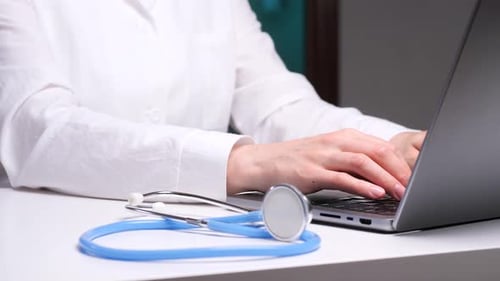 Doctor Typing on Laptop in Office, Stethoscope Nearby