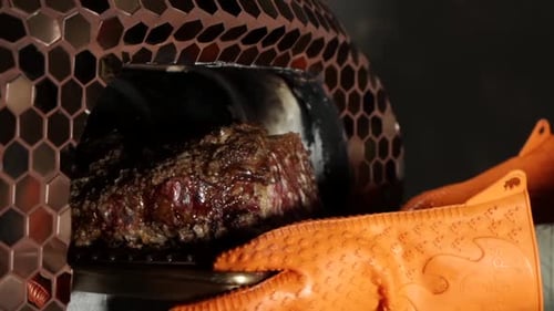Close-up shot of a well-cooked beef joint out of an oven with oven mitts
