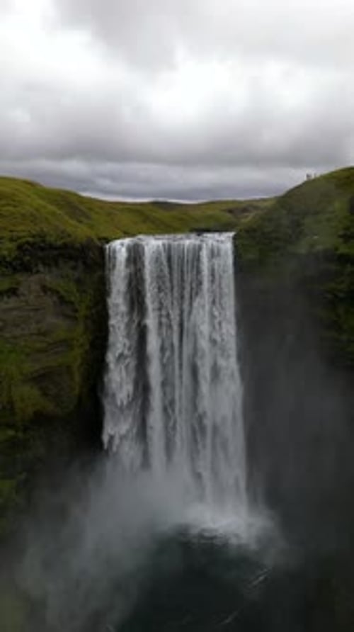 cinematic drone footage of Skógafoss Waterfall in Iceland, capturing the immense curtain of water