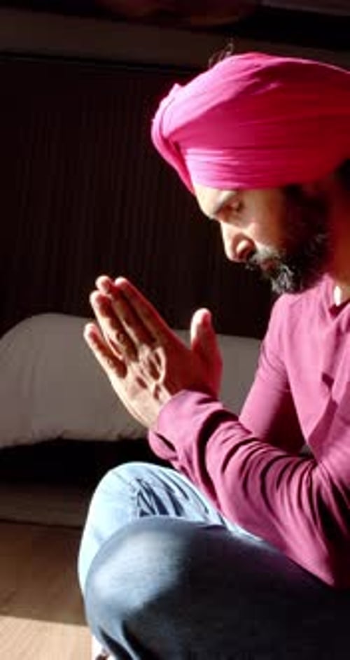 Vidéo verticale : Priant les mains jointes, homme en turban en tenue traditionnelle assis à la maison