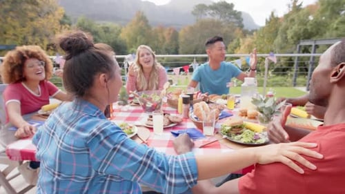 Happy diverse group of friends eating and talking at dinner table in garden, slow motion