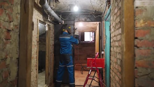 Back Shot of Professional Welder in Safety Suit and Protective Mask Welds Metal Door Using Welding