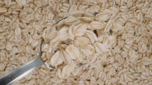 Oat flakes on a metal spoon viewed from above against a background of oats, looped as an advertising