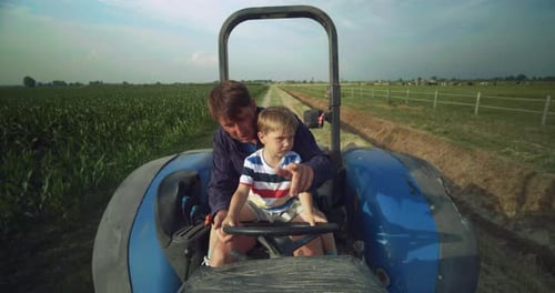 Portrait of Young Man and His Toddler Son Driving Tractor on Warm Summer Day in a Corn Field. Littl