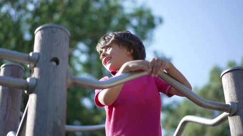 Young boy smiling while holding onto metal bars of playground structure, enjoying a carefree moment