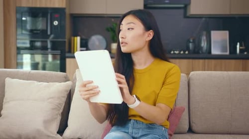 Close Up Young Asian Woman Sitting on Couch in Cozy Room Use Tablet Device Smile at Home
