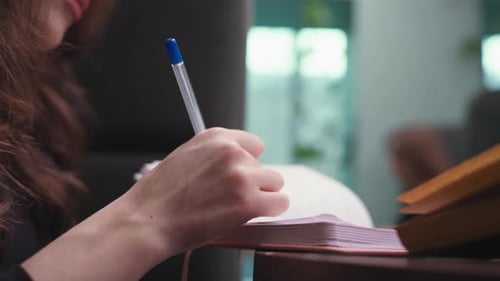 Person Writing in Notebook with Blue Pen