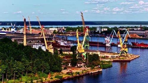Luftaufnahme eines Industriehafens mit Frachtkränen, angedockten Schiffen, Lagerhäusern und Wäldern