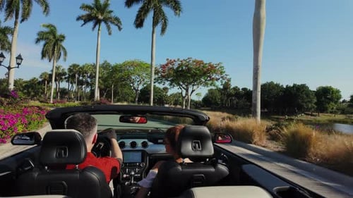 Paar fährt rotes Cabrio und winkt mit den Händen unter den Handflächen, Rückseite, Weitwinkelaufnahme