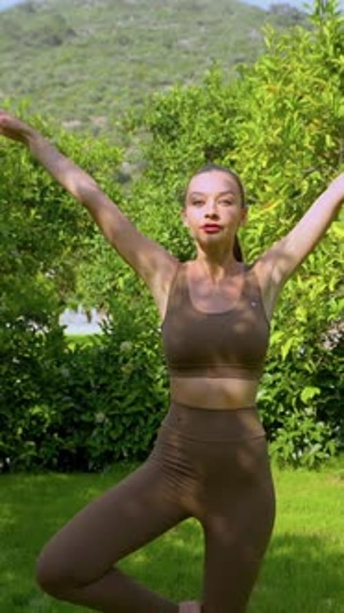 Femme pratiquant la pose de yoga Vrksasana dans un jardin verdoyant avec des montagnes en arrière-plan
