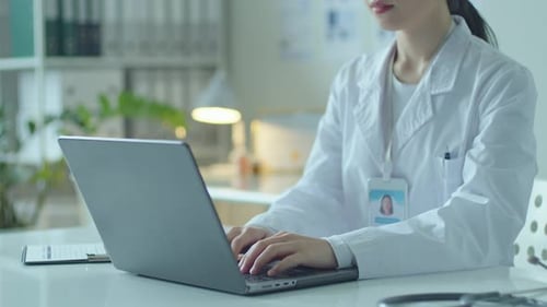 Female Doctor Typing on Laptop at Desk in Medical Office