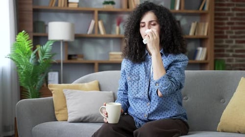 Woman with Curly Hair Sitting on Sofa Blowing Nose
