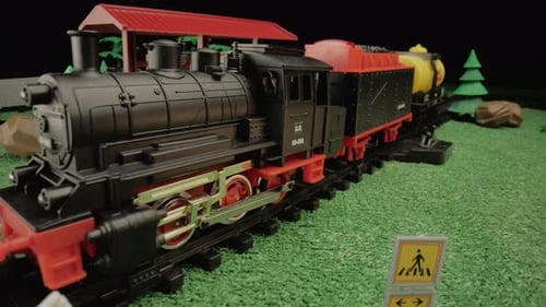 Modell einer Kunststoff-Dampfbahn für Kinder mit Güterwagen, die auf einem Bahnsteig inmitten einer Grünanlage stehen