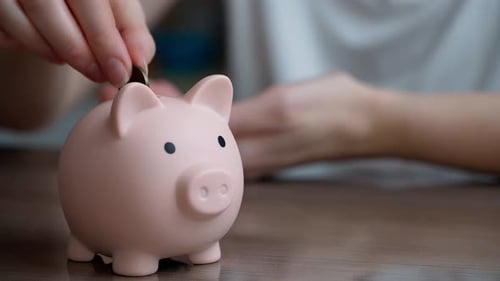 Eine junge Frau spart Geld in einem Sparschwein für Ersparnisse.