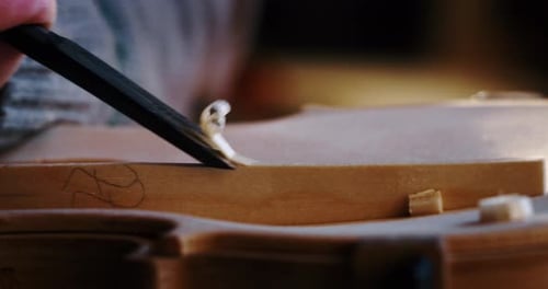 Slow motion macro of master artisan luthier painstaking detailed work on wood violin in a workshop